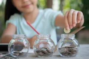 Niña colocando una moneda en un frasco, representando el ahorro y la educación financiera.