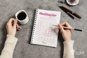 Persona usando una plantilla impresa de meditación diaria tipo challenge de 25 días, creada por La EJE, con taza de café y bolígrafo.