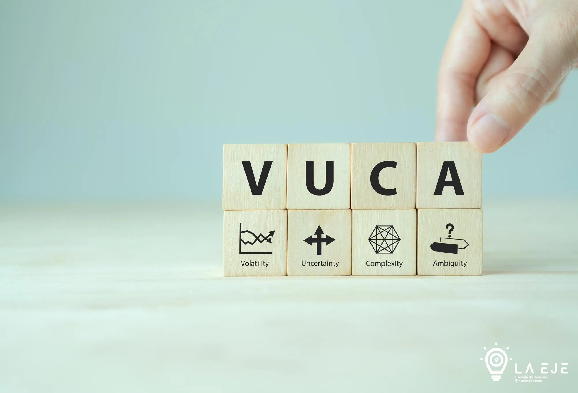 Bloques de madera con las letras VUCA y sus significados: volatilidad, incertidumbre, complejidad y ambigüedad, junto al logo de La EJE.